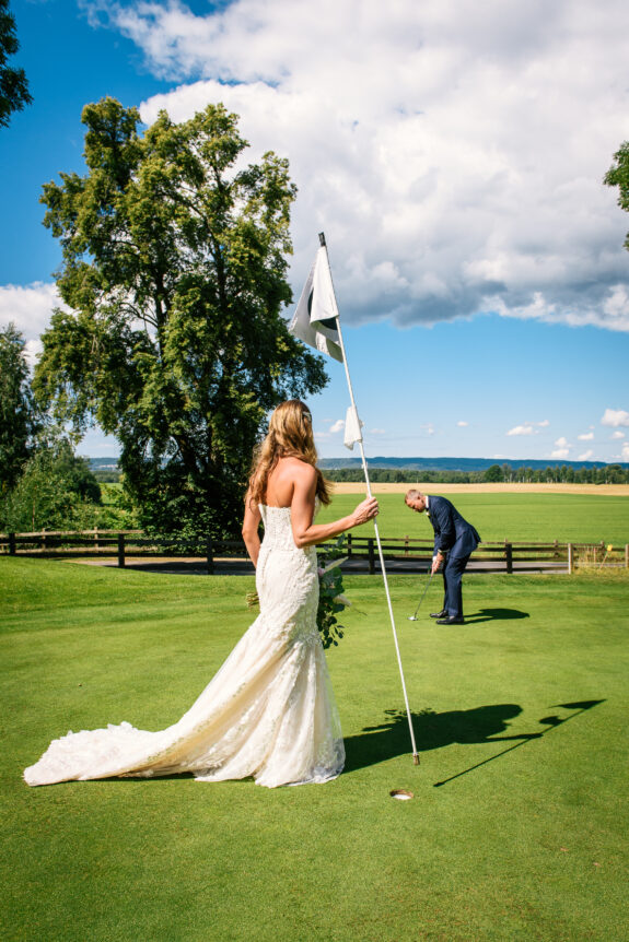 En man i kostym spelar golf i Skaraborg med sin fru i vit klänning.